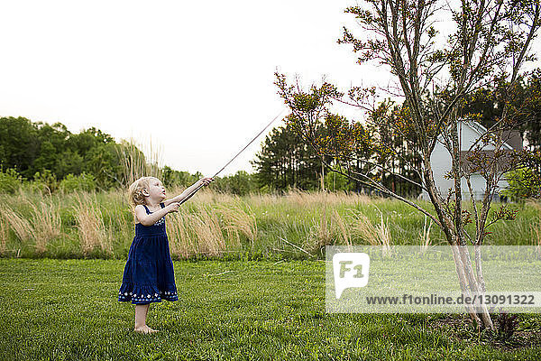 Girl playing with stick while standing on grassy field against clear sky