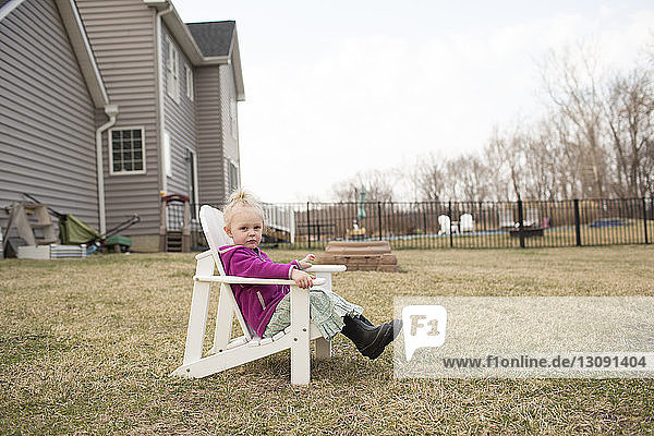Portrait of cute girl sitting on chair in backyard against clear sky