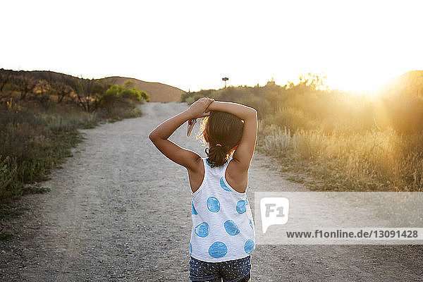 Rear view of girl standing on road against clear sky on sunny day