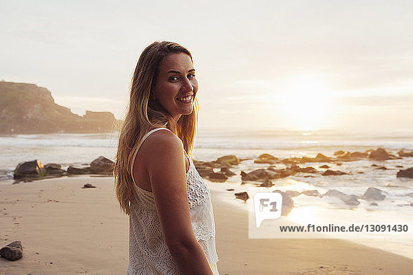 Porträt einer lächelnden Frau  die bei Sonnenuntergang am Strand steht