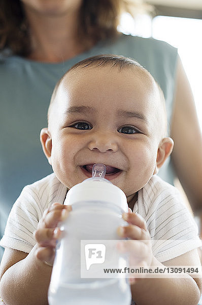 Porträt eines lächelnden kleinen Jungen  der die Flasche hält  während er bei der Mutter sitzt