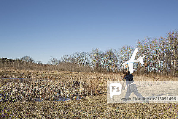 Playful boy flying model airplane while standing on field against clear sky