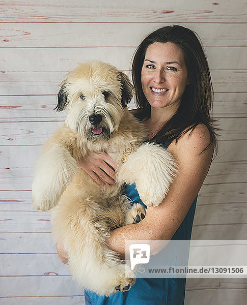 Porträt einer glücklichen Frau  die einen Hund trägt  während sie vor einem Vorhang steht