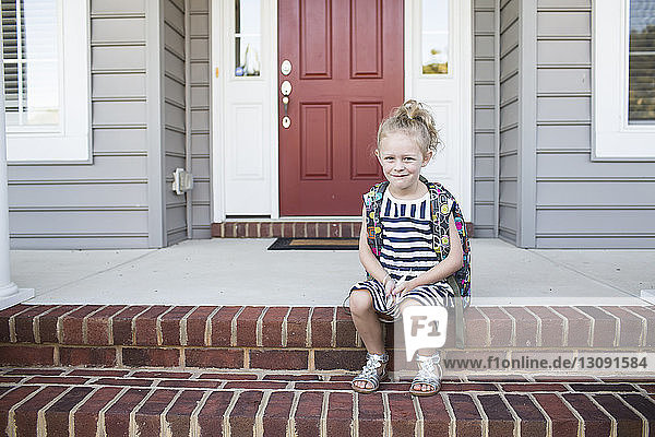 Porträt eines Schulmädchens  das auf Stufen vor dem Haus sitzt