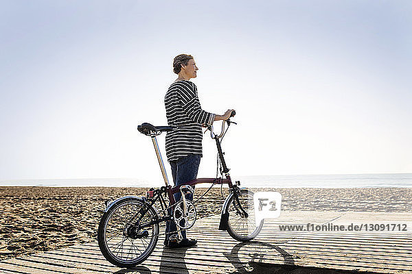 Frau mit Fahrrad auf Fußweg am Strand vor klarem Himmel