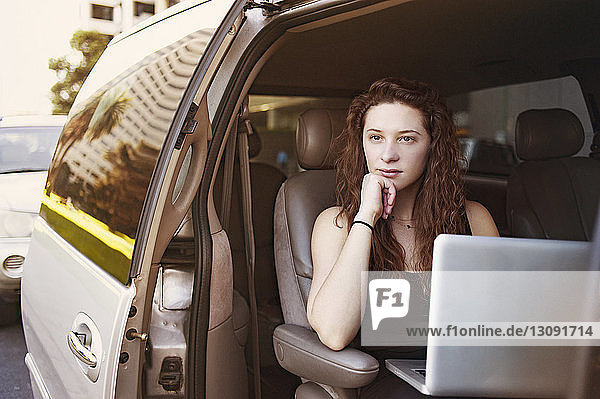 Nachdenkliche junge Frau sitzt mit Laptop im Auto
