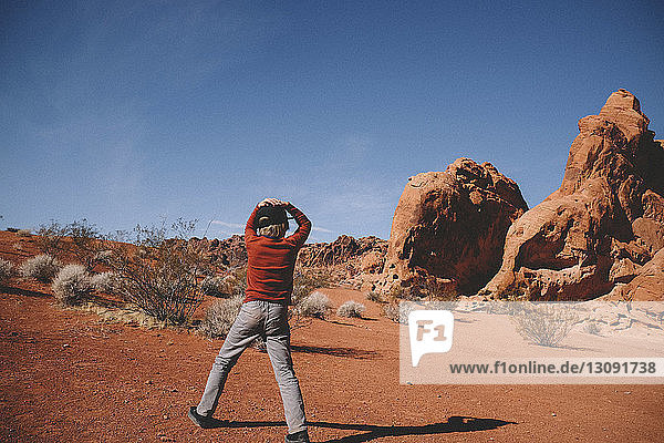 Boy standing against rock formations and sky at Valley of Fire State Park during sunny day