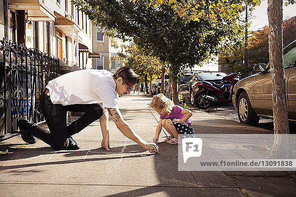 Vater und Tochter beim Zeichnen des Hüpfspieles auf dem Fußweg