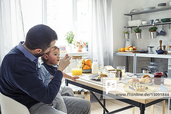 Father feeding breakfast to son at table in kitchen