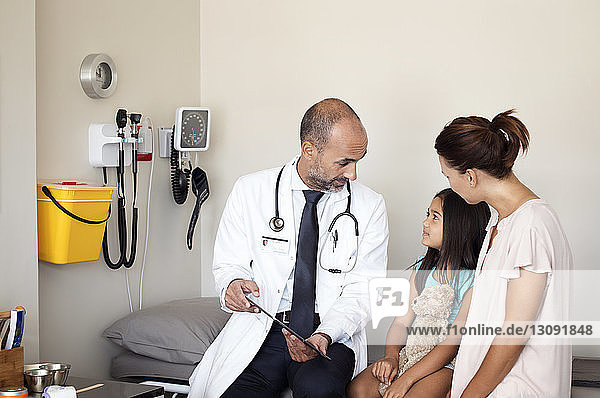 Mother and doctor looking at daughter while sitting in medical examination room