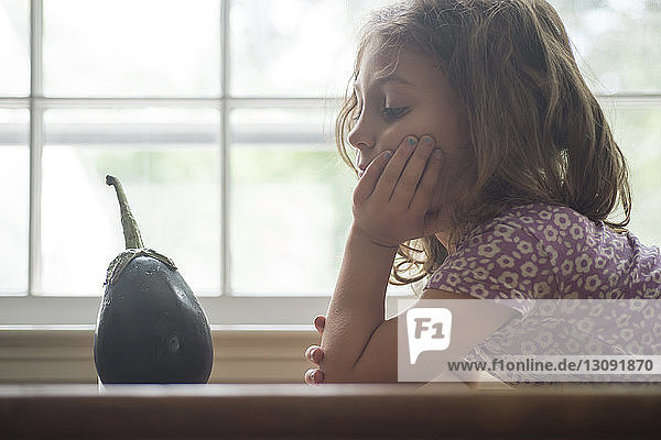 Bored girl looking at eggplant by window in home