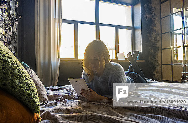 Teenager-Mädchen schaut auf Tablet-Computer  während sie zu Hause im Bett liegt