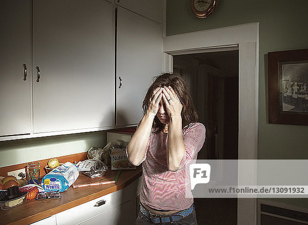 Frau mit Kopfschmerzen in der Küche stehend