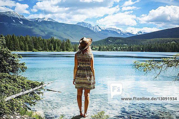 Rückansicht einer Frau mit Hut  die auf einem Felsen am See im Jasper-Nationalpark steht