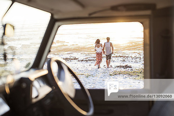 Rückansicht eines am Strand spazieren gehenden Paares durch das Fenster eines Geländewagens gesehen