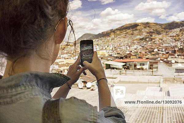 Rückansicht einer Frau  die ein Wohnviertel mit einem Smartphone gegen den Himmel fotografiert