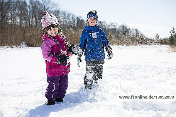 Playful siblings enjoying on snow covered field against sky