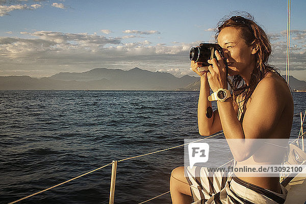 Frau fotografiert  während sie im Boot auf dem Meer gegen den Himmel sitzt