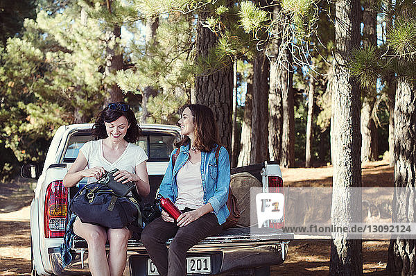 Happy female friends talking while sitting on pick-up truck in forest
