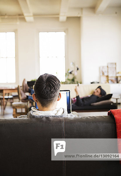 Geschäftsmann mit Laptop  während ein Kollege im Kreativbüro auf dem Sofa liegt