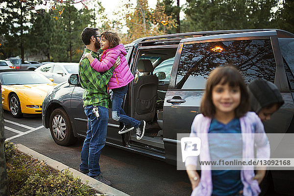 Mann hilft Tochter beim Aussteigen aus dem Auto mit Kindern im Vordergrund
