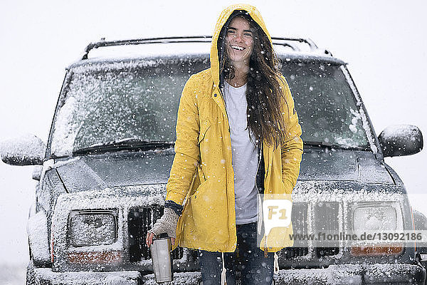 Portrait of cheerful woman standing by off-road vehicle on field during winter
