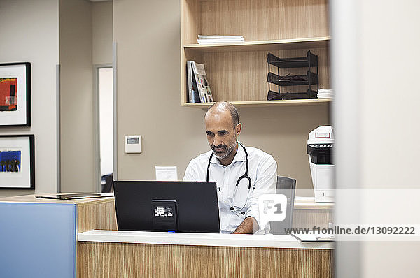 Arzt mit Desktop-Computer bei der Arbeit im Krankenhauszimmer durch Glas gesehen