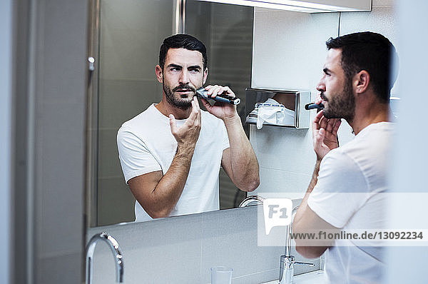 Mann benutzt elektrischen Rasierapparat im Badezimmer eines Hotelzimmers