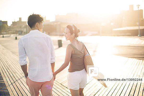 Rückansicht eines Paares  das sich beim Gehen auf dem Pier an den Händen hält
