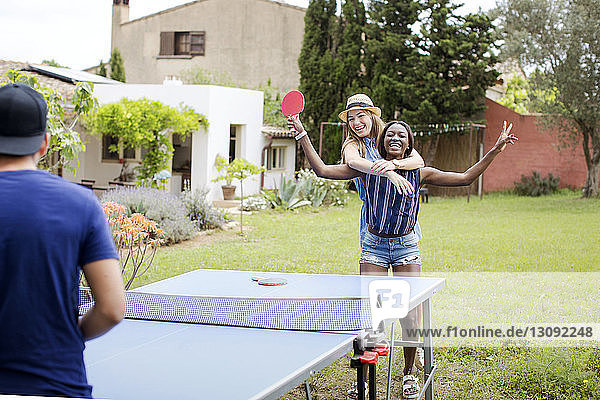 Fröhliche Frauen spielen Tischtennis mit einem Freund auf dem Hof