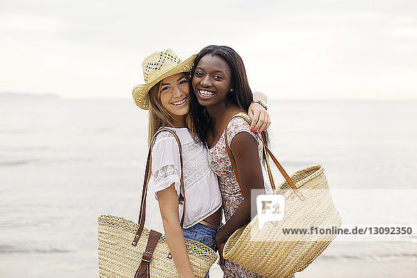 Side view portrait of happy female friends embracing while standing on shore at beach