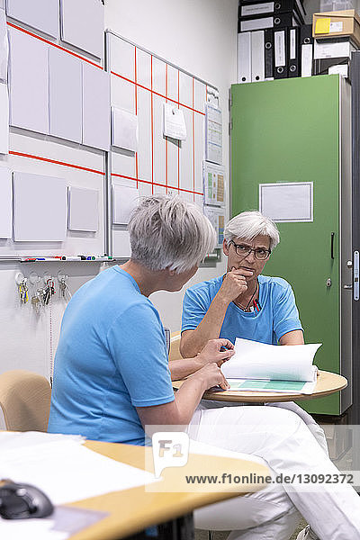 Female doctors discussing medical records while sitting in medical clinic