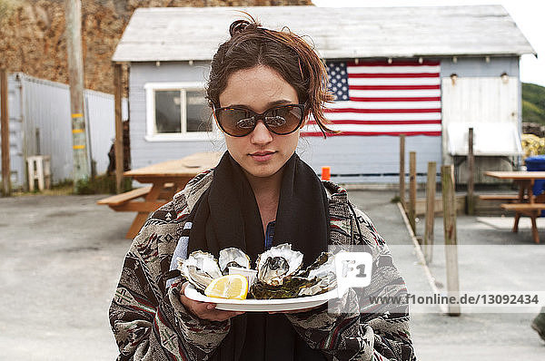 Frau hält Austern im Teller vor dem Haus