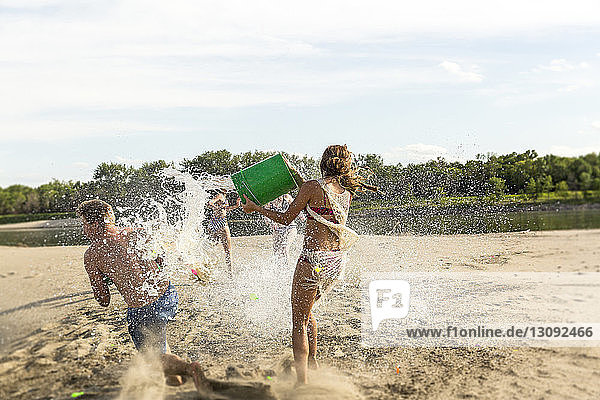 Freunde spielen mit Wasser am Strand gegen den Himmel