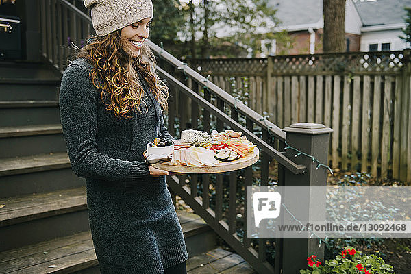 Frau trägt Essen auf Holzbrett im Hinterhof