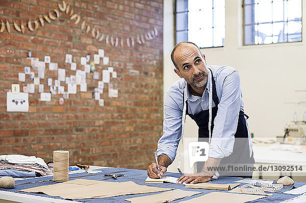 Männlicher Modedesigner schaut weg  während er am Tisch in der Werkstatt arbeitet