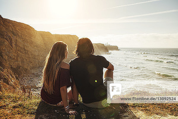 Rear view of couple sitting on cliff and looking at sea