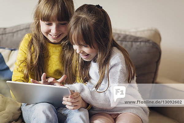 Sisters looking into tablet computer while sitting at home