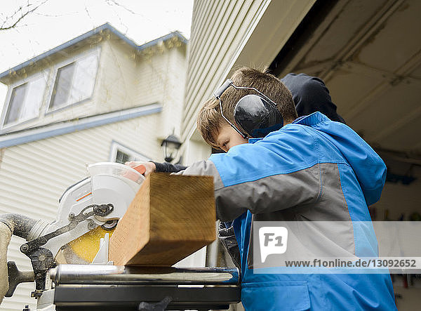 Side view of boy using ear protectors while working at backyard