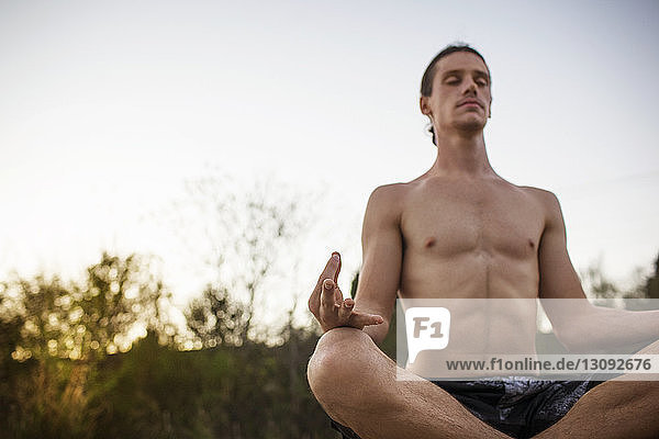 Mann praktiziert Yoga in Lotus-Position bei klarem Himmel