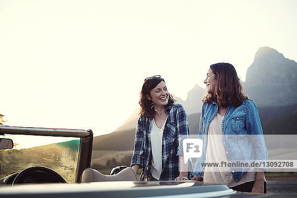Freundinnen unterhalten sich  während sie bei einem Cabriolet vor klarem Himmel stehen