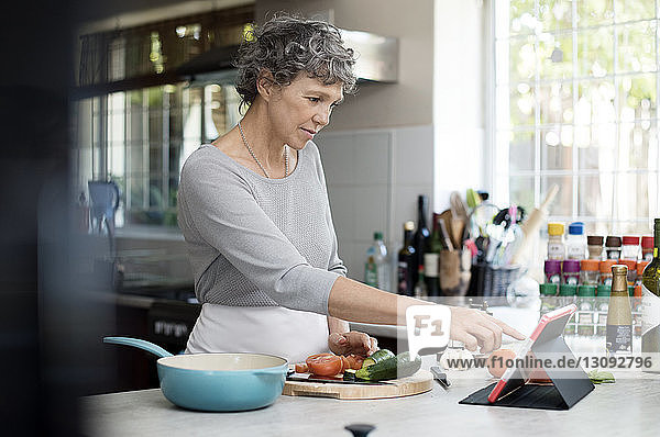 Reife Frau benutzt digitale Tablette beim Kochen in der Küche
