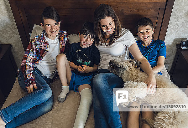 Schrägaufnahme einer glücklichen Mutter mit Söhnen und Hund  die zu Hause auf dem Bett sitzen