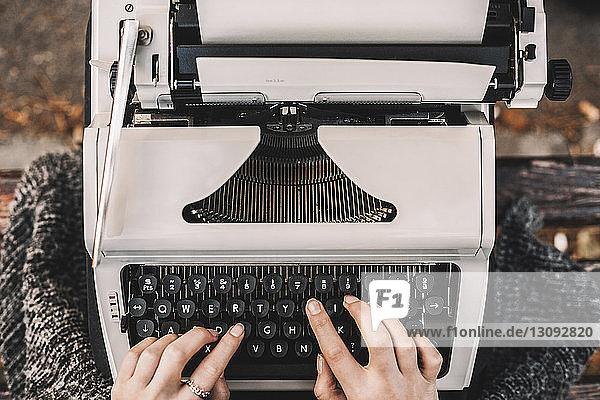 Beschnittenes Bild einer Schriftstellerin  die auf einer Parkbank sitzend mit der Schreibmaschine schreibt