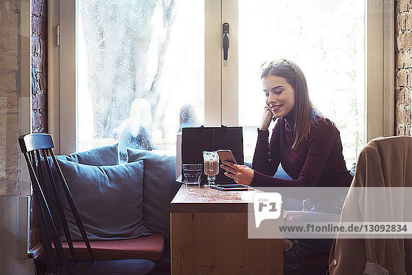 Frau benutzt Mobiltelefon  während sie im Cafe am Fenster sitzt