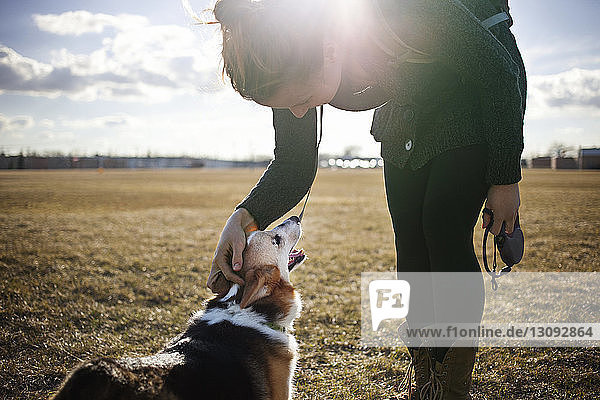 Woman playing with dog on field against sky on sunny day