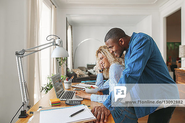 Side view of smiling couple using laptop computer at home office