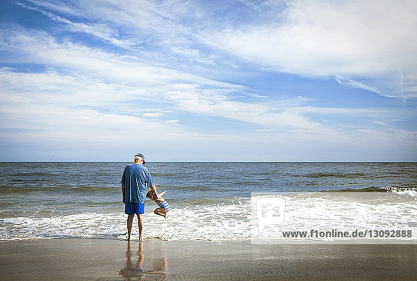 Großvater steht neben einem Mädchen  das am Strand am Ufer spielt
