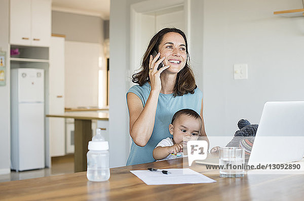 Frau spricht mit Smartphone  während sie mit ihrem Sohn zu Hause sitzt