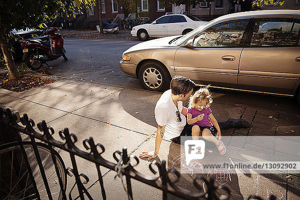 Vater sieht Tochter an  während er auf dem Fußweg sitzt